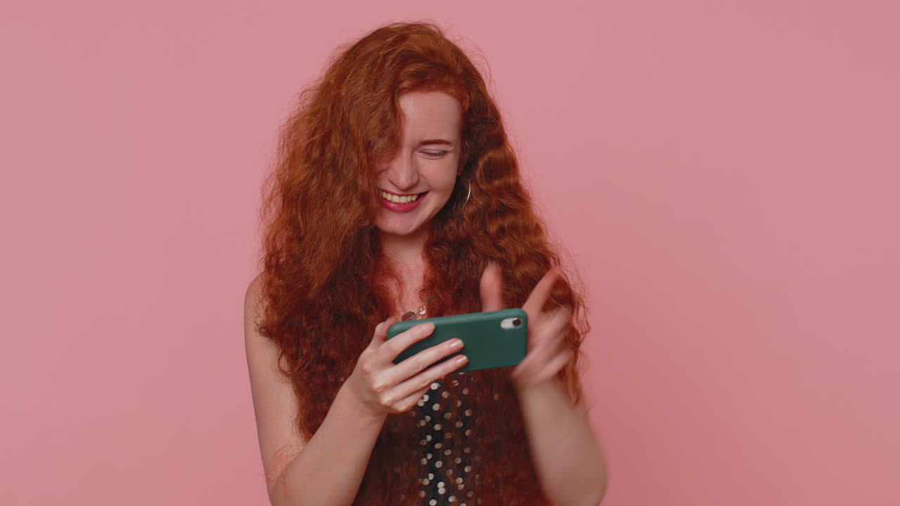 Preoccupata, divertente, dipendente, rossa, gioca con entusiasmo a un videogioco di corse sul cellulare.