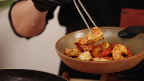 chef usando una pinza de cocina, agarre, levante y transfiera los camarones cocidos de la sartén a un tazón, toma de cámara lenta