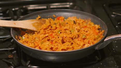 spicy seasoned mexican rice cooking gently in frying pan on gas hob in kitchen with chicken, peppers, onions with steam rising in slow motion. dinner ready to serve to friends and family 4k.