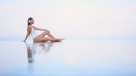 Posied-on-the-edge-of-an-infinity-pool-a-beautiful-young-woman-turns-to-the-camera-and-smiles