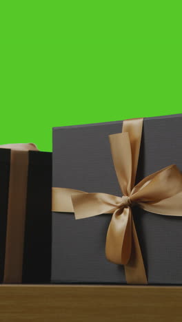 vertical video of presents in gift wrapped boxes decorated with ribbon on table shot against green screen