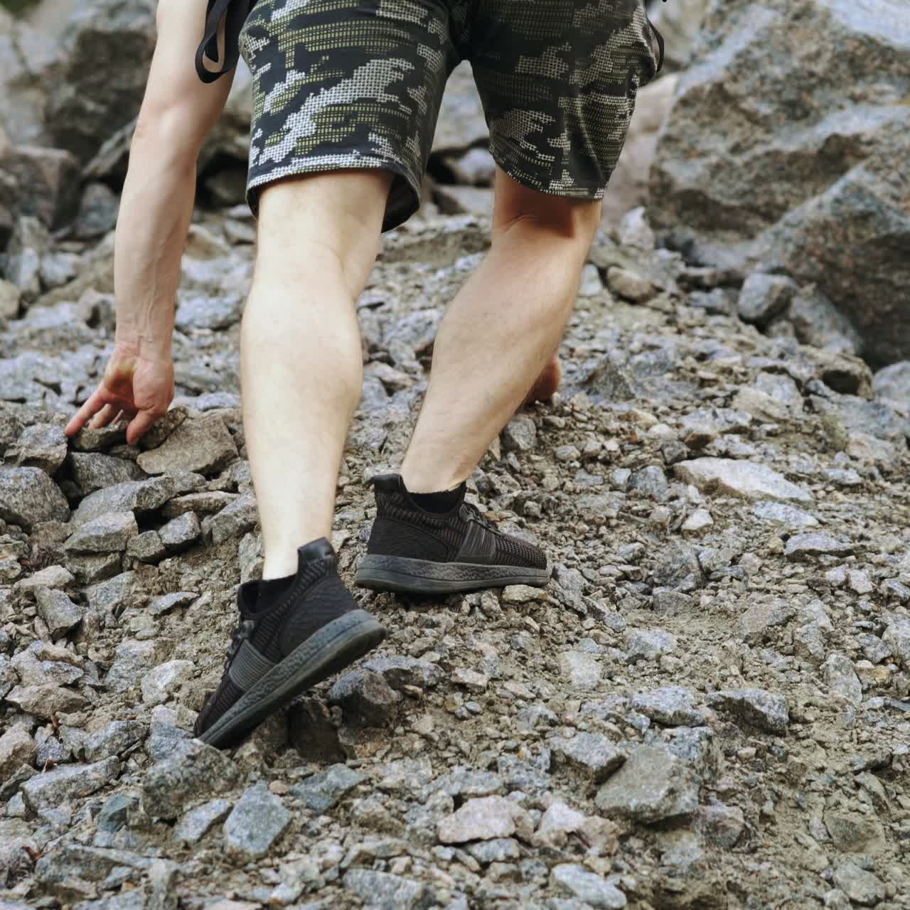 tourist with a backpack and in sneakers is climbing using his hands to the top of the cliff in the summer