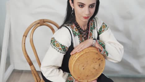 el retrato muestra a una hermosa mujer joven en auténtica ropa bordada ucraniana adornada con adornos tradicionales sosteniendo una gran pieza redonda de queso