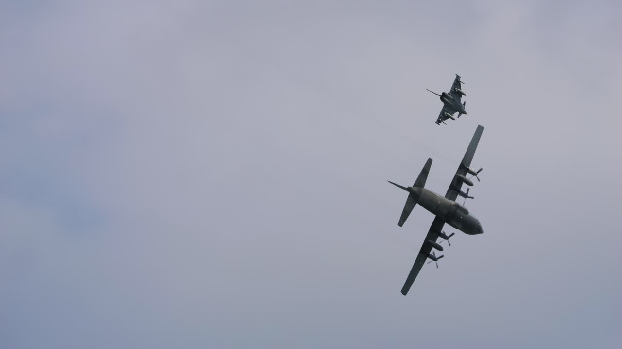 Airbus A400M aircraft and the eurofighter fly close to each other at the Airpower airshow, tracking across open blue sky