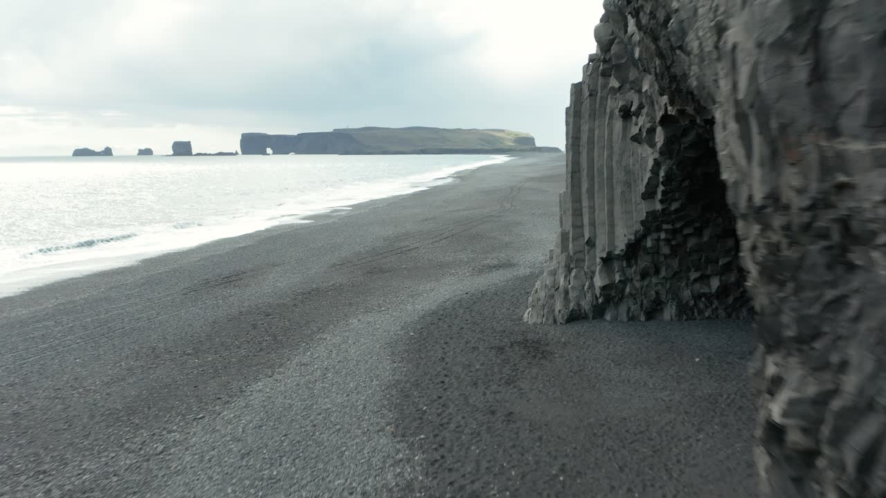 acantilado de basalto de reynisdrangar en reynisfjara playa negra y distante dyrhólaey