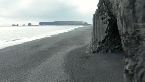 basalt cliff of reynisdrangar at reynisfjara black beach and distant dyrhólaey