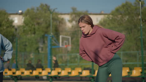 young girls performing outdoor workout with blurred background of people in the distance, engaged in fitness activity at sports court, enjoying sunlight and exercise