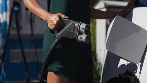 sección media de una mujer caucásica cargando un coche eléctrico
