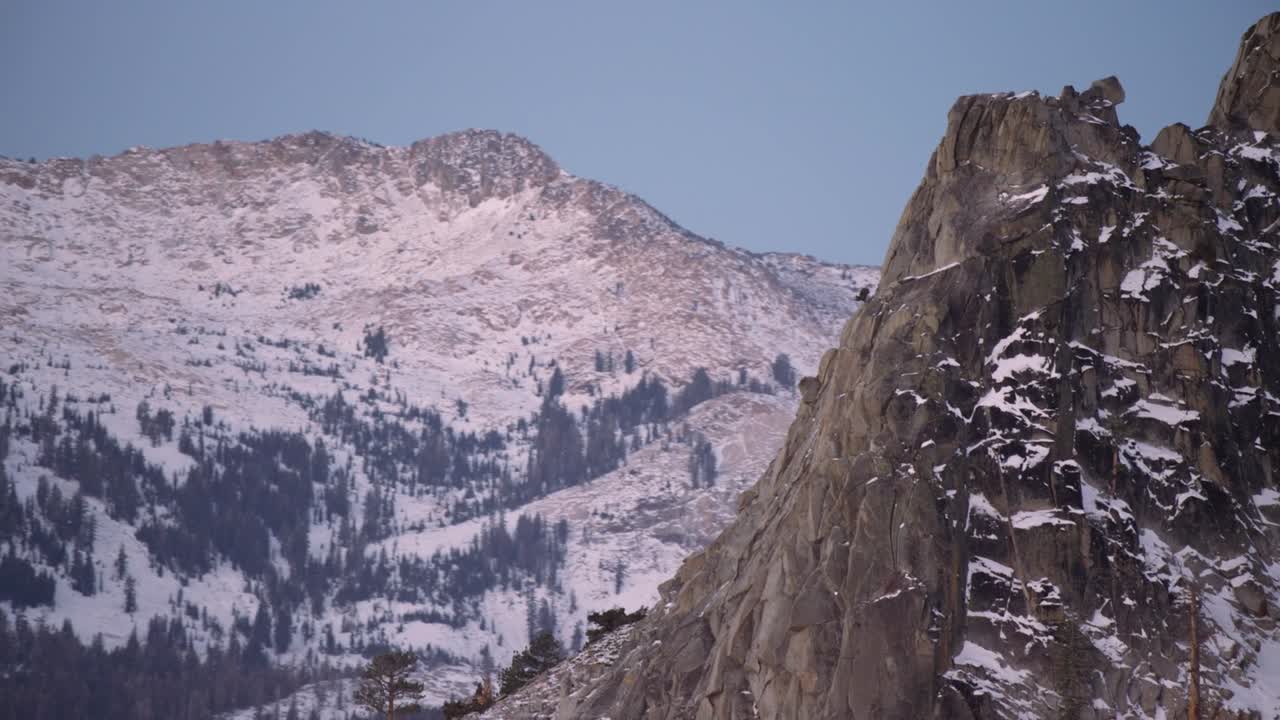 Filmato in time-lapse di un drammatico paesaggio montano caratterizzato da ripide scogliere rocciose con chiazze di neve in primo piano. Vaste cime e creste innevate si estendono sullo sfondo.