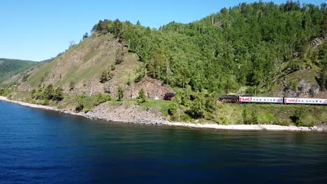 close approach passengers train trans siberian railway brick bridge. lake baikal coast. summer beautiful holiday russia. sunny day green field high rocks. fast speed aerial drone 4k footage.