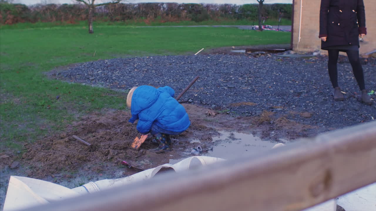 A little kid shovelling mud in a backyard in the countryside. STATIC SHOT