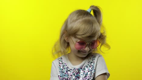 Child-smiling,-looking-at-camera.-Girl-tourist-in-pink-sunglasses-posing-on-yellow-background