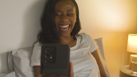 young couple at home at night lying in bed looking at mobile phones together 2