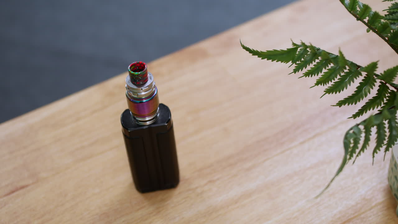 A man picking up an electronic cigarette vape from a table desk as he is leaving home