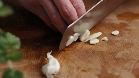 Male-chef-sliceing-garlic-in-thin-slices-in-the-kitchen-on-a-wooden-cutting-board-in-the-kitchen