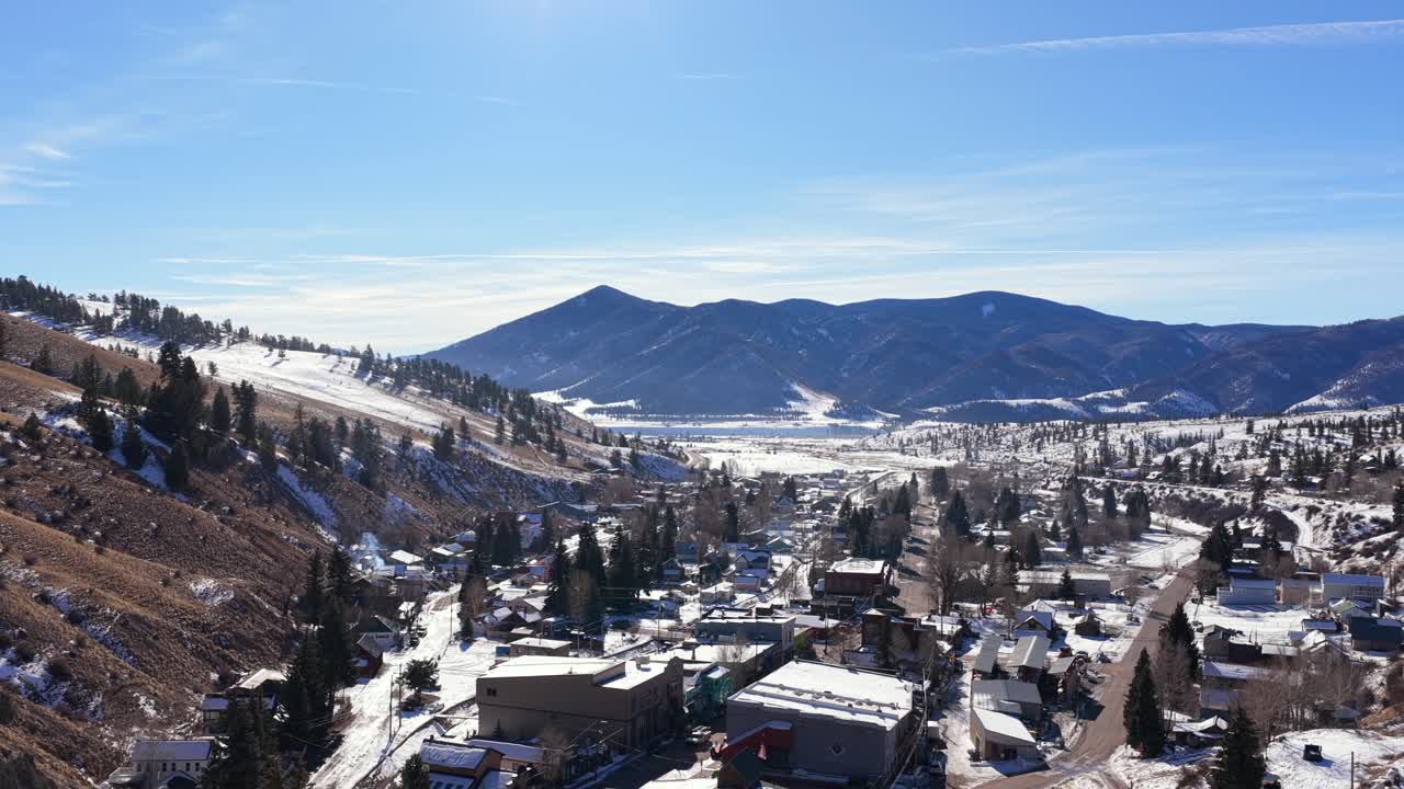 Una spettacolare rivelazione con drone supera un'imponente parete rocciosa a picco per svelare un remoto villaggio di montagna. Il villaggio innevato si trova in una profonda valle alpina, circondato da una selvaggia natura invernale.
