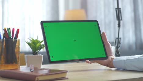 vista de arriba hacia abajo de una computadora portátil con pantalla verde simulada pantalla chromakey en un escritorio de oficina de madera al lado de la libreta con bolígrafos, gafas y un vaso de agua.