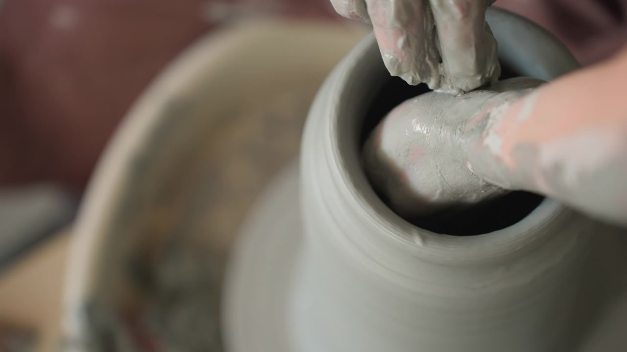 Steady wheel turning with control. Maintaining consistent rhythm while shaping pottery. Focused demonstration emphasizes gentle and steady movements during clay centering process on wheel