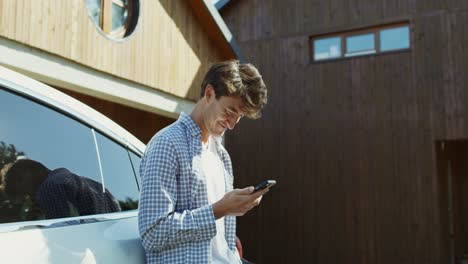 hombre enviando mensajes de texto en su teléfono inteligente cerca de un coche eléctrico