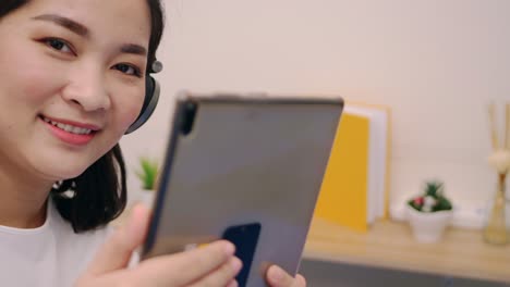 Beautiful-asian-woman-look-camera-and-smile-relaxing-and-listening-to-music-by-tablet-with-headphones-on-the-bed-at-home-lifestyle-and-pleasure-concept