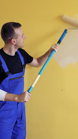 room renovations at home. painter man starts painting wall with a roller on a long handle. professional painting services, contractor. vertical video