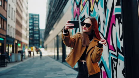 stylish young woman posing with phone against vibrant graffiti wall