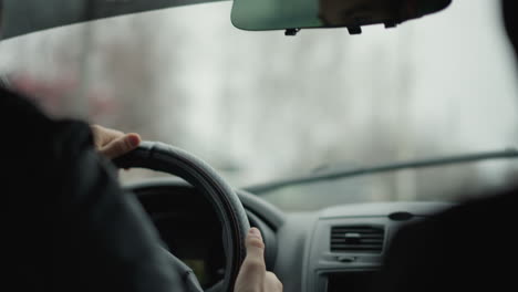 window cleaner wiping water from front glass while driver navigates rainy urban road, wet windshield and wiper motion visible through raindrops, focus on driver hand on steering wheel and city