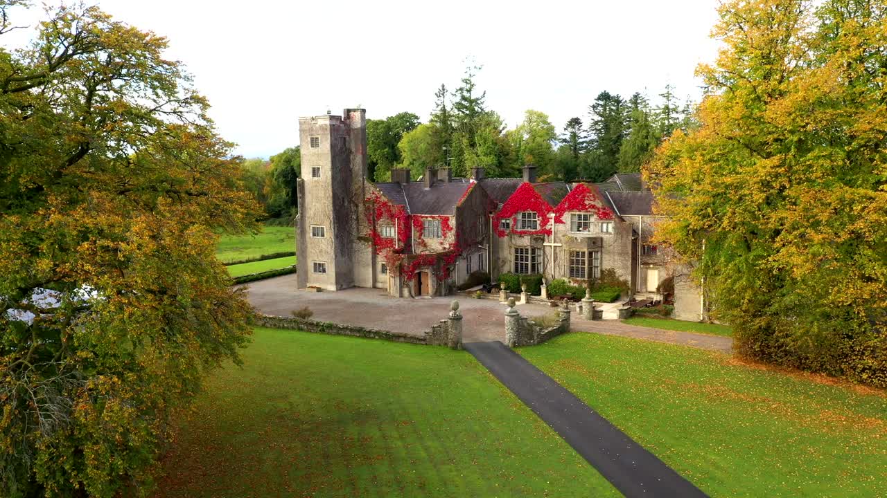 Castle viewed from entrance path lined with trees in full fall color, drone orbit reveal