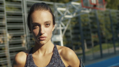 close up of a sporty woman smiling cheerfully at the camera while standing at sport court on a summer day