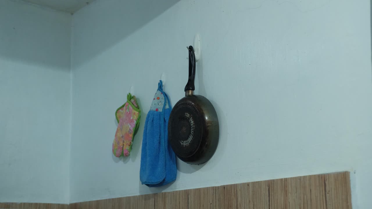 Static shot of young man placing frying pan on wall hanger in apartment kitchen.