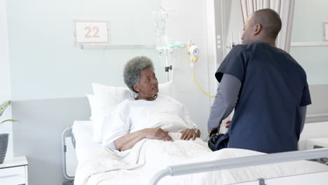 african american male doctor talking with female senior patient in hospital room, slow motion