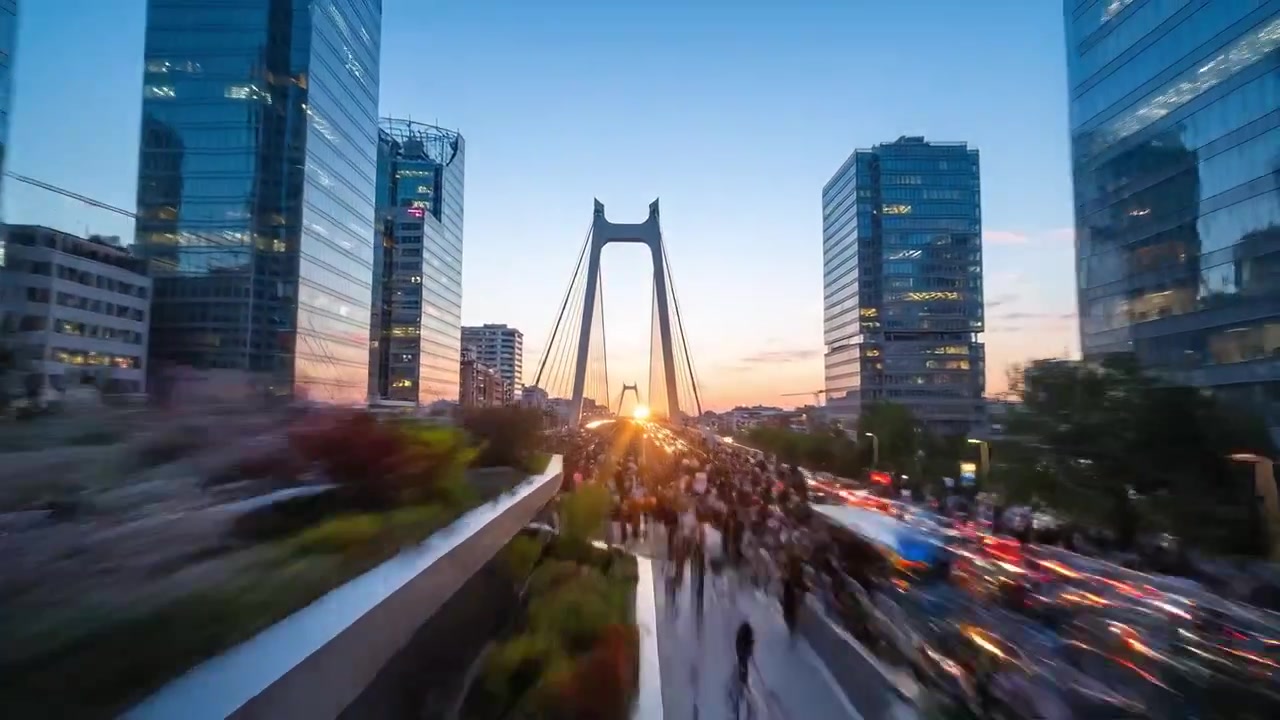 Dynamic urban scenery featuring vibrant traffic and bustling pedestrians at dusk beneath a modern bridge illuminated by the golden glow of sunset.