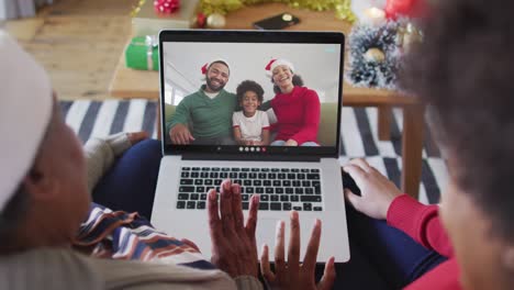 African-american-mother-and-daughter-using-laptop-for-christmas-video-call-with-family-on-screen