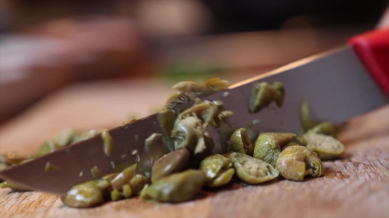 Tritare i capperi con un coltello su un tagliere di legno.