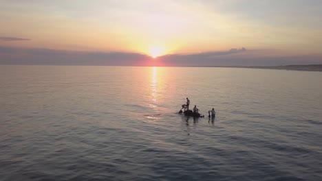 aerial view - the sun falls on the horizon while these guys have fun on an abandoned boat, uruguay, rocha, la paloma