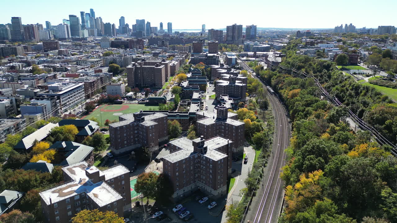 descubra el paisaje dinámico de hoboken, nueva jersey, mientras un tren de tránsito de nj se mueve a través del cuadro en esta toma de drone de paralaje con el icónico horizonte de la ciudad de nueva york en el fondo.