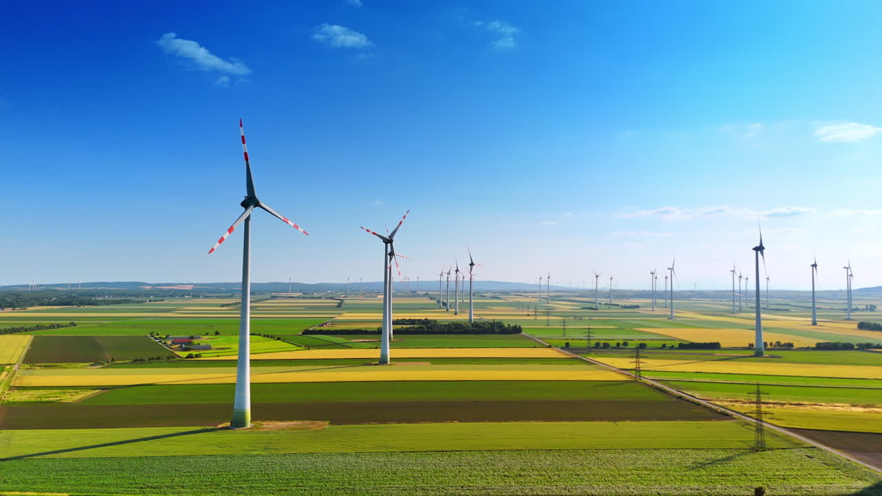 Wind turbines by farmland. Vast fields of green and yellow show multiple wind turbines generating clean energy under a clear blue sky