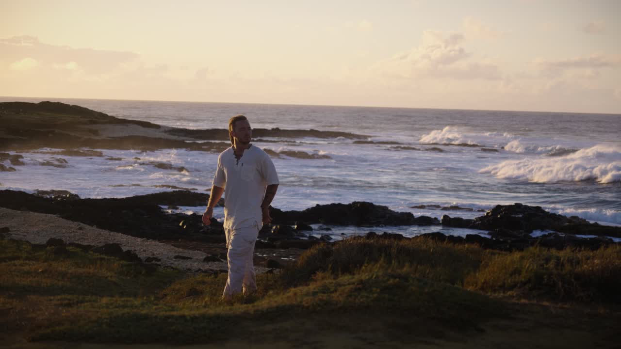 A lone woman sits by the ocean as waves crash against black rocks beneath the soft glow of sunset, capturing solitude and reflection by the sea