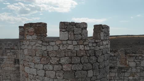 close up view of the walls of an ancient castle, as the camera rises up and reveals the surrounding fields and hills