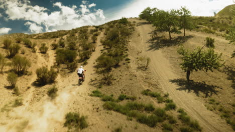 motorbiker rides vehicle leaving dust trail in hilly valley. sportsman maneuvers motorcycle uphill competing in racing on hot day. power of speed