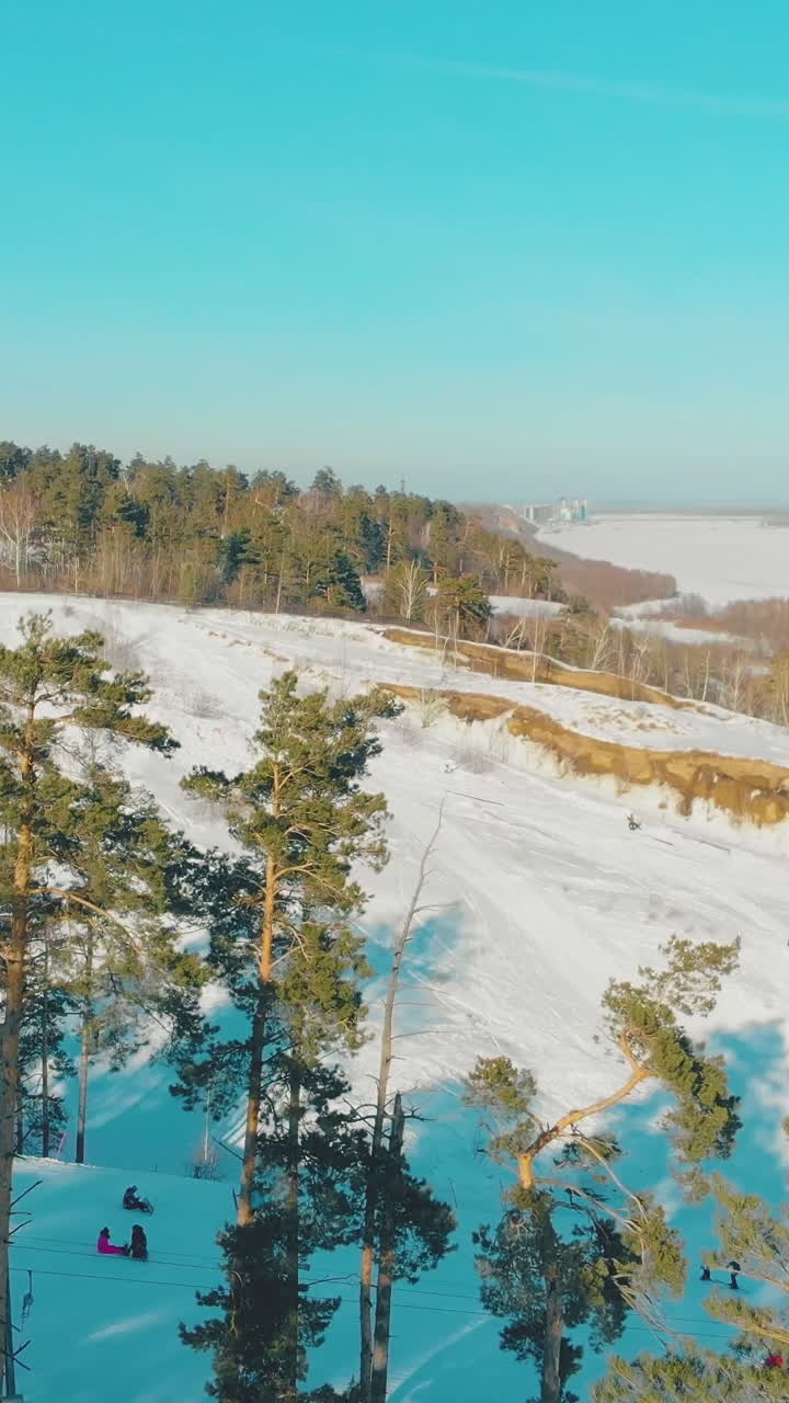 aerial motion above snowy mountains with downhill skiers at modern resort on nice sunny winter day