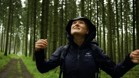 happy woman hiking through a forest in the rain. taking a deep breath in the woods. disconnecting from the world and taking a walk in a forest.