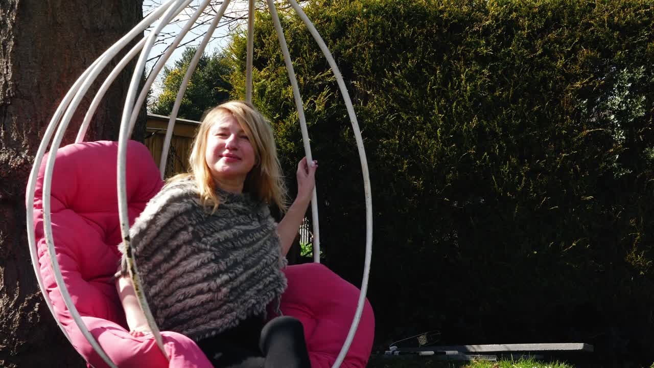 Donna attraente che si rilassa su un dondolo da giardino, zoom medio, al rallentatore