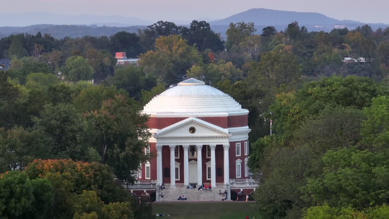 The Rotunda Building in USA with relaxing students in park area. University of Virginia during autumn season. Aerial approaching shot.