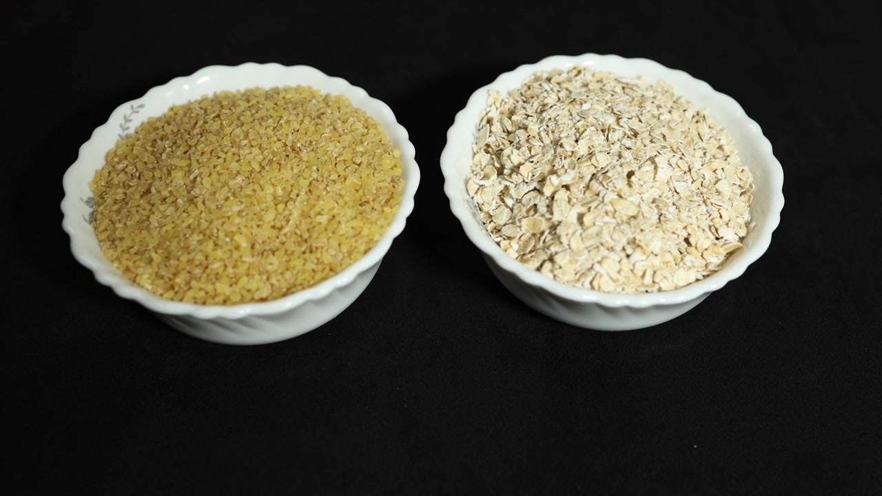 Grano spezzato e fiocchi d'avena in ciotole di ceramica isolati su sfondo nero.