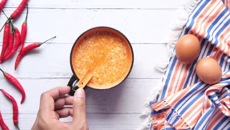 hand holding spoon over a bowl of egg drop soup with chilies and eggs