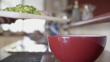 a chef scraping sliced spring onion into a red mixing bowl