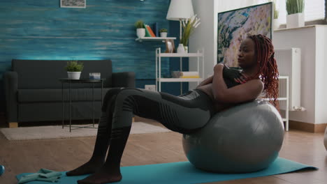 Slim-fit-black-woman-sitting-on-yoga-swiss-ball-doing-abs-exercise