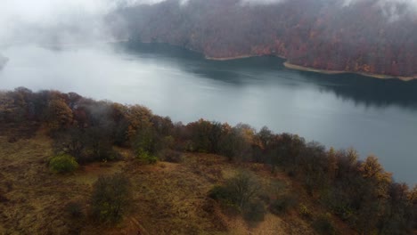 Aerial-descent-from-rain-cloud-toward-mountain-lake-in-autumn-colours