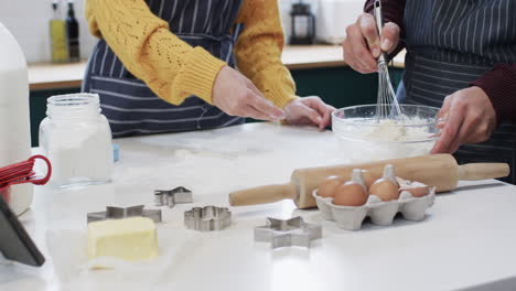 Midsection-of-diverse-couple-baking-christmas-cookies-in-kitchen-at-home,-in-slow-motion